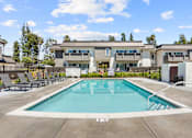 Thumbnail 53 of 91 - A swimming pool in front of a building with a fence and trees in the background.