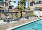 Thumbnail 48 of 91 - A pool with lounge chairs and a sign in front of apartment buildings.