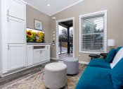 Thumbnail 32 of 97 - New Apartments In South Austin - Casata Austin - Spacious Living Room With Wood-Inspired Plank Flooring, Area Rug, Couch, Round Stools, Side Table With Lamp, High Ceilings, Built-In White Cabinets, TV, Window With Blinds, And Access To Patio