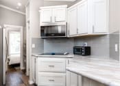 Thumbnail 33 of 97 - 2-Bedroom Apartments in South Austin, TX - Casta Austin - Kitchen with Built-In Stainless Steel Microwave, Marble-Style Countertop, Grey Tile Backsplash, and White Cabinetry.