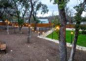 Thumbnail 70 of 97 - South Austin Apartments - Casata Austin - Gated Dog Park With Benches, String Lighting, And Trees