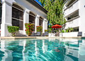 Thumbnail 32 of 48 - A pool with a red umbrella and chairs in front of a white building.
