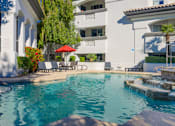 Thumbnail 40 of 48 - A pool with a red umbrella and a white building in the background.