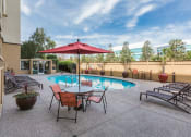 Thumbnail 14 of 86 - Studios in Redwood City, CA - Avenue Two - Heated Outdoor Pool with Lounge Chairs, Potted Palm Trees, and Fence at Avenue Two Apartments, California