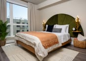 Thumbnail 29 of 89 - Pet-Friendly Apartments In South Park Los Angeles CA - Emerald - A Spacious And Bright Bedroom With A Full-Size Bed In The Center With One Wall Featuring A Nearly Floor-To-Ceiling Window, Wood-Style Flooring, Area Rug, And Lightly Colored Walls