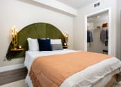Thumbnail 30 of 89 - One-Bedroom Apartments in South Park Los Angeles, CA - The Emerald - Furnished Bedroom with Green Headboard, Spacious Closet, and Luxury Plank Flooring