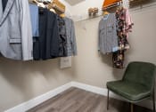 Thumbnail 32 of 89 - a walk in closet with a chair and clothes hanging on the wall