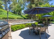 Thumbnail 15 of 27 - a patio with a grill and tables with umbrellas at 55+ FountainGlen Laguna Niguel, Laguna Niguel, CA, 92677