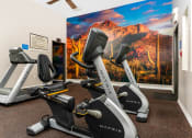 Thumbnail 31 of 34 - two exercise bikes in a gym with a wall mural of mountains at 55+ FountainGlen Valencia, California