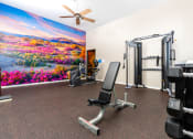 Thumbnail 29 of 34 - a gym with exercise equipment and a painting of flowers on the wall at 55+ FountainGlen Valencia, Valencia, California