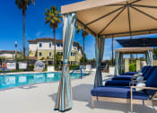 Thumbnail 13 of 34 - a pool with blue lounge chairs and a tan umbrella next to a pool at 55+ FountainGlen Valencia, Valencia, CA, 91354
