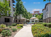 Thumbnail 26 of 34 - A sunny day at a courtyard with a pathway, plants, and umbrellas. at 55+ FountainGlen Terra Vista, Rancho Cucamonga, 91730