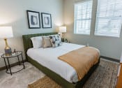 Thumbnail 6 of 83 - Bayswater Burlingame - Spacious Bedroom With Plush Carpet Flooring, Area Rug, Bed, Nightstands With Lamps, Dresser, Wall Art, And Two Windows With Blinds at Bayswater Apartments, Burlingame, CA