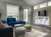 Thumbnail 24 of 97 - Brand New Apartments In South Austin, TX - Casata Austin - Living Room With Couch, Chair, Wood-Style Flooring, Three Ottomans, Area Rug, TV Stand With TV, And Five Windows.