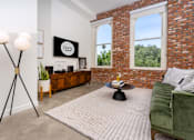 Thumbnail 41 of 68 - a living room with a green couch and a brick wall at Imperial Hardware Lofts, Riverside, CA