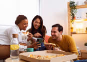 Thumbnail 14 of 60 - a group of people sitting around a table eating pizza and looking at a cell phone
