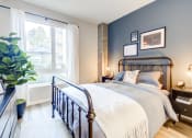 Thumbnail 3 of 18 - Downtown Oakland, CA Luxury Apartments Near Lake Merritt - Edson House - Bedroom With Floor Plant, Luxury Wood Finish Plank Flooring, Large Window, Concrete Pillar, Two Nightstands, and a Bed.