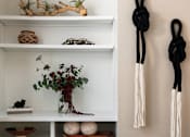 Thumbnail 25 of 33 - A white shelf with various decorative items and two black and white tassels hanging on the wall.
