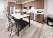 Thumbnail 17 of 24 - a kitchen with a table and a refrigerator Pet-Friendly Apartments in Walnut Creek - NoMA - Kitchen with Wood Cabinetry, Plank Luxury Flooring, Quartz Countertops and Stainless Steel Appliances at NoMa
