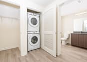 Thumbnail 27 of 52 - A white washer and dryer are stacked in a small laundry room.