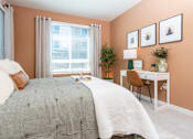 Thumbnail 33 of 93 - 2 Bedroom Luxury Apartments in Riverside, CA - North Grove - Cozy Bedroom With Large Window And Curtains, Soft Bedding, Accent Pillows, And Workspace Desk Beside Seating Chair