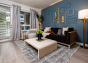 Thumbnail 37 of 93 - Luxury Apartments in Riverside, CA with In-Unit Washer and Dryer - North Grove - Inviting Living Room With Blue Accent Wall, Sofa, Floor Lamp, Coffee Table, And Sliding Glass Door With Drapes