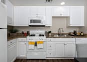 Thumbnail 7 of 112 - A white kitchen with a stove top oven and a microwave above it.