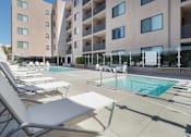 Thumbnail 8 of 26 - A pool area with sun loungers and a building in the background at Wilshire Valencia Apartment, Los Angeles, CA