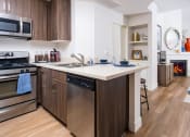 Thumbnail 15 of 59 - Miracle Mile Los Angeles, CA Apartments for Rent - The Preston - Kitchen with Plank Wood Style Flooring, Stainless-Steel Appliances, Granite-Style Countertops, and Breakfast Bar.