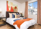 Thumbnail 22 of 59 - Two-Bedroom Apartments in Los Angeles, CA - The Preston - Bedroom with Plank Wood Style Flooring, Large Bed, Nightstands with Lamps, and Spacious Window.