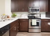 Thumbnail 11 of 84 - Apartments in Mission Valley CA - The Promenade Rio Vista - Kitchen with Wood-Style Flooring, Dark Brown Cabinets, Ceramic Tile Countertops, Subway Tile Backsplash, and Stainless Steel Appliances