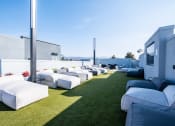 Thumbnail 17 of 18 - Downtown Oakland, CA Luxury Apartments Near Fox Theater - Edson House - Meditation Deck With Multiple Lounge Chairs, Faux Grass, Mounted Tv, and Two Large Light Posts.