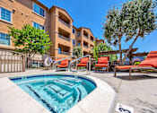 Thumbnail 7 of 40 - Two-Bedroom Apartments in San Jose, CA - Aviara - Spa with Orange Lounge Chairs, Trees, and Apartment Building in the Background.