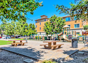 Thumbnail 13 of 40 - a park with a playground and picnic tables in front of a building