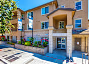 Thumbnail 3 of 40 - Apartments for Rent in San Jose, CA - Aviara - Street View of Property with Tan Building Exterior, Manicured Plant Beds, and Sidewalk.