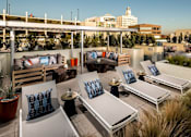 Thumbnail 16 of 25 - A rooftop patio with lounge chairs and cushions overlooking a cityscape.at Chelsea Santa Monica, Santa Monica California  