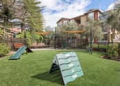 Thumbnail 15 of 36 - Gated Dog Park With Manicured Grass, Climbing Equipment, Benches, Shaded Areas, Surrounding Trees, And View Of Apartment Building at Montrachet Apartments, California, 94558