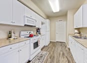Thumbnail 1 of 19 - Two-Bedroom Apartments in Upland, CA - Park Central Apartments - Kitchen with Wood-Style Flooring, White Cabinetry, White Appliances, and Ceiling Light.