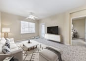 Thumbnail 3 of 19 - 2-Bedroom Apartments in Upland, CA - Park Central Apartments - Living Area with Carpet Flooring, Couch, Ottoman, Coffee Table, Side Table, Floor Lamp, Ceiling Fan, Media Console, and Television.