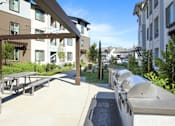 Thumbnail 25 of 87 - A bbq patio area with tables and chairs is surrounded by apartment buildings.