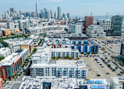 Thumbnail 45 of 50 - A cityscape with a mix of modern and older buildings, a parking lot, and a body of water in the distance.