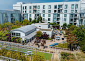Thumbnail 43 of 50 - A modern building with a grey roof is surrounded by trees and other buildings.