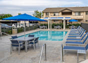 Thumbnail 22 of 39 - a swimming pool with blue chairs and umbrellas and a building in the background at Sunstone Place, Riverside, California