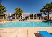 Thumbnail 31 of 142 - A swimming pool with a blue lounge chair and a building in the background.