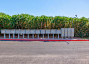 Thumbnail 52 of 142 - A parking lot with a row of parking meters and a hedge in the background.