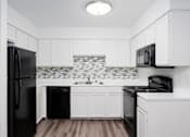 Thumbnail 122 of 142 - A black refrigerator is in a kitchen with white cabinets.