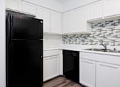 Thumbnail 124 of 142 - A black refrigerator in a kitchen with white cabinets and a black dishwasher.