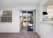 Thumbnail 112 of 142 - A room with a carpeted floor, a window with blinds, and a sliding glass door leading to a balcony.