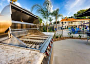 Thumbnail 25 of 27 - A large outdoor grill is in the foreground with a patio and pool in the background at Nola 624 Apartments, California, 91790