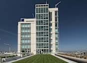 Thumbnail 3 of 104 - A modern building with a glass facade and a green lawn in front at The Grand Apartments, Oakland 94612